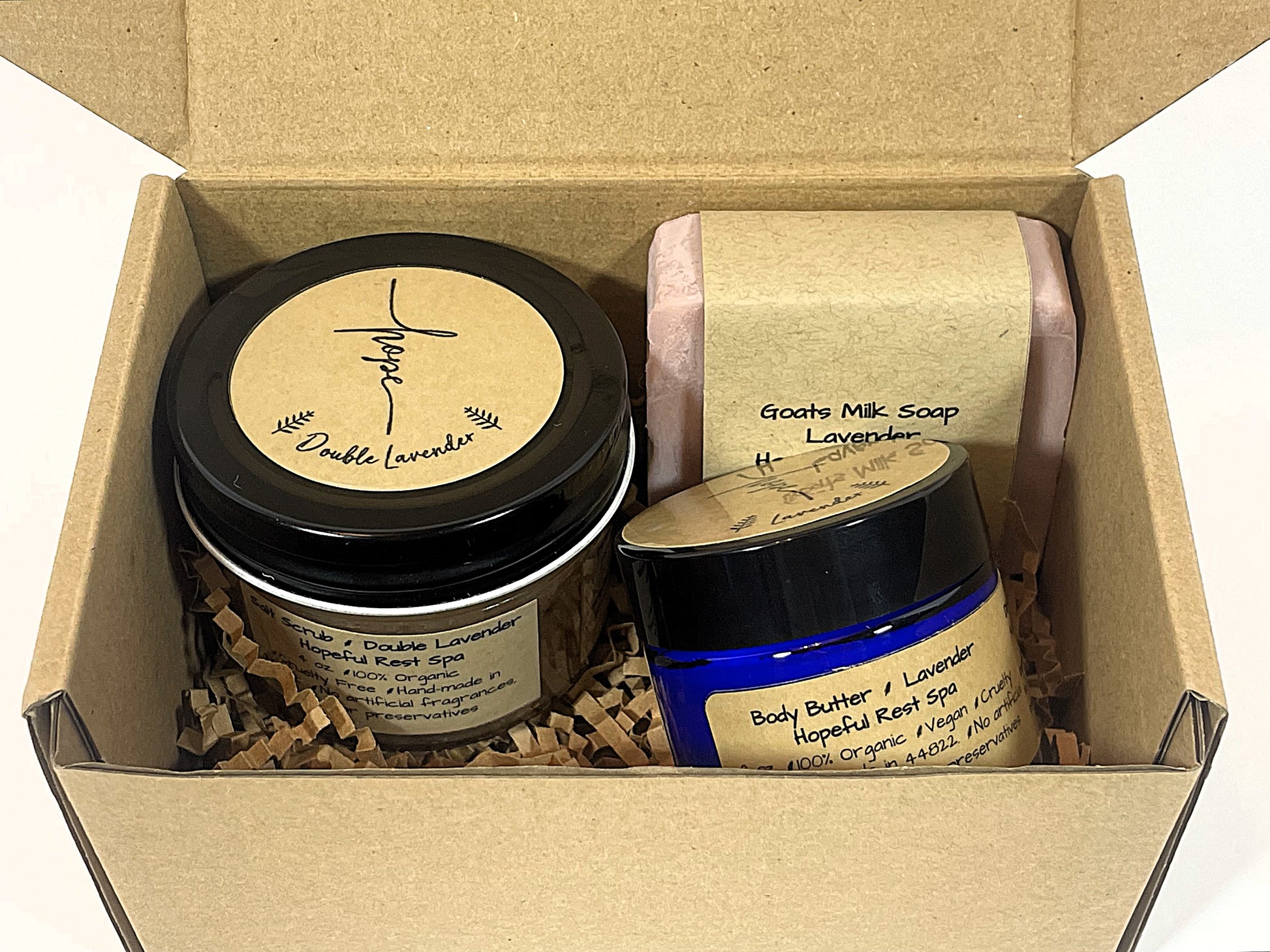 A gift set including a jar of lavender goats milk bar soap, a pink salt scrub, and a jar of 2 oz. lavender body butter, all with labels and placed in a box
