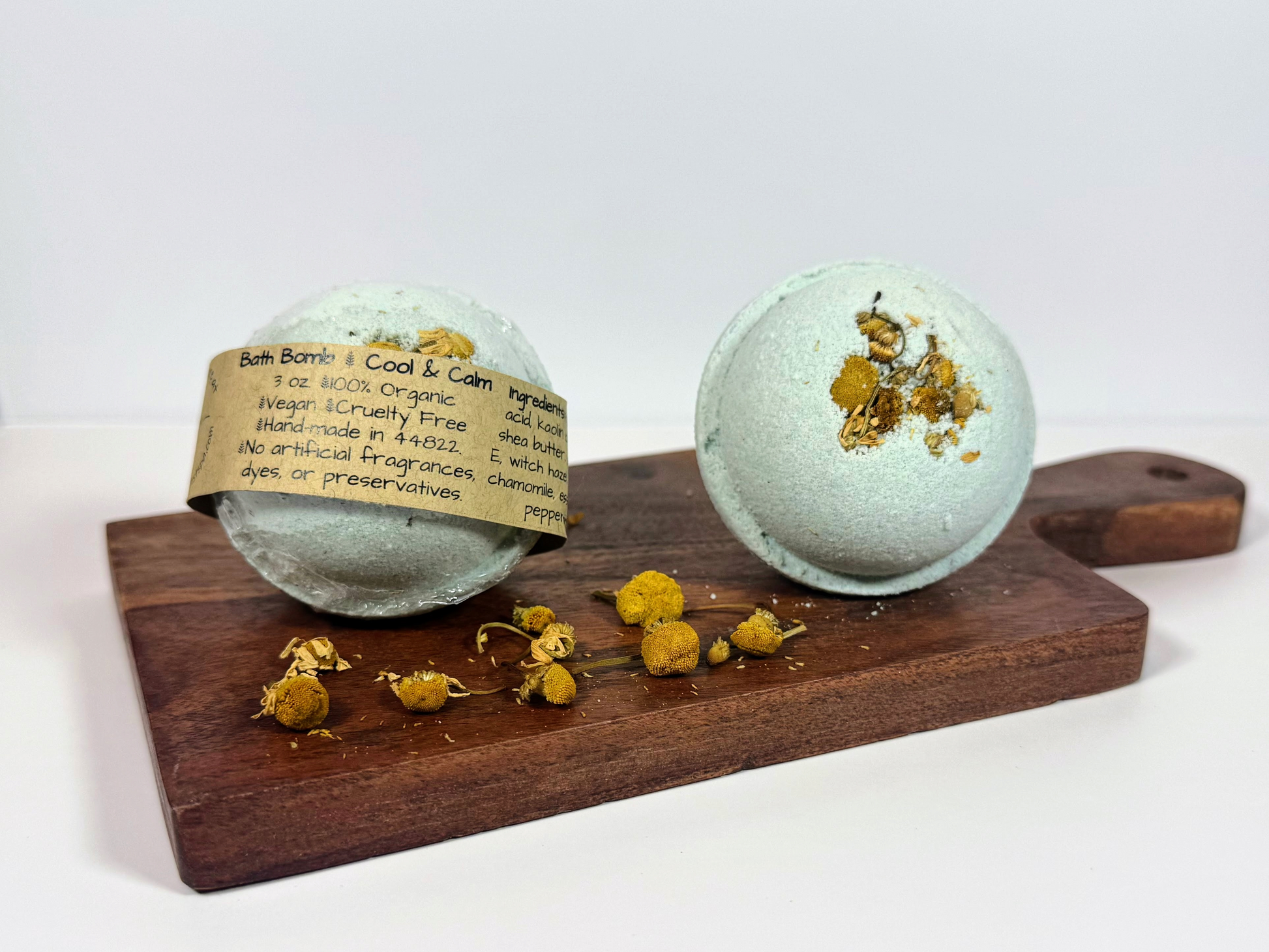 Two bath bombs with Chamomile flowers on a wooden board against a white background