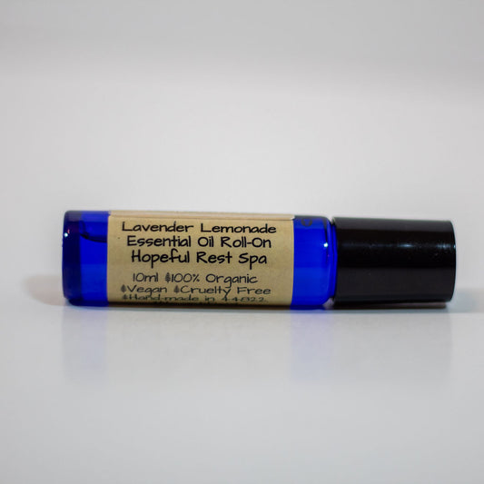 A 10ml essential oil roll-on bottle with a cobalt blue glass body, a black cap, and a beige paper label that reads 'Lavender Lemonade Essential Oil Roll-On Hopeful Rest Spa'.