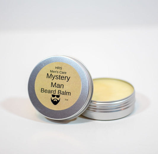 An open silver metal tin of HRS Men's Care Mystery Man Beard Balm, showing the pale yellow balm inside, with the lid resting beside it on a white background.